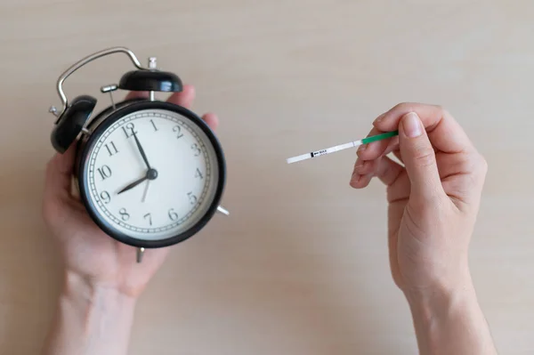 La mujer tiene una prueba de embarazo negativa y un despertador. Concepto de reloj biológico de fertilidad femenina. Una tira . — Foto de Stock