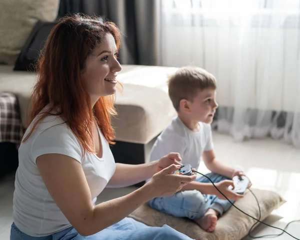 Gelukkige vrouw en zoon spelen videospelletjes thuis. Een gokker en zijn moeder spelen met de joysticks van de spelcomputer in hun handen. Een gelukkig gezin. — Stockfoto