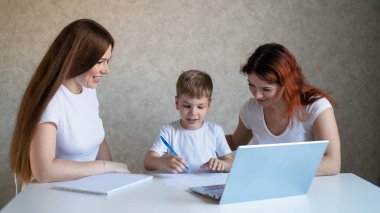 İki kadın çocuğa okul ödevinde yardım ediyor. Bayan öğretmen, evde bir çocuğa mutfakta ders veriyor. Öğretmen bireysel bir ders veriyor. Anne oğlunun çalışmasına yardım eder..