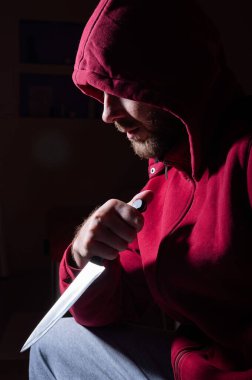 Kırmızı başlıklı tehlikeli sakallı bir adam yüzüne yakın bir bıçak tutuyor. Bir suçlu ya da karanlıkta bıçaklı bir katil..