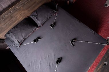 Bedroom for intimate meetings. VDSM equipment and sex toys. Leather handcuffs with a chain on a gray sheet. Fifty shades of gray. Fetish domination. clipart