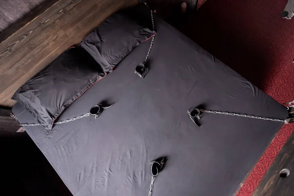 Bedroom for intimate meetings. VDSM equipment and sex toys. Leather handcuffs with a chain on a gray sheet. Fifty shades of gray. Fetish domination.