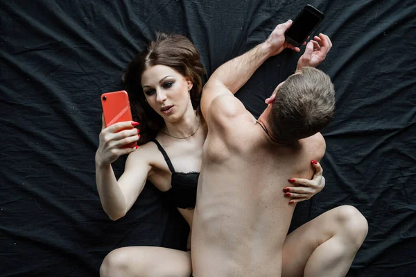 Um casal se envolve em olhar para seus telefones celulares enquanto faz sexo. Tédio e falta de atração durante o cumprimento do dever conjugal. vício em smartphones e redes sociais . — Fotografia de Stock