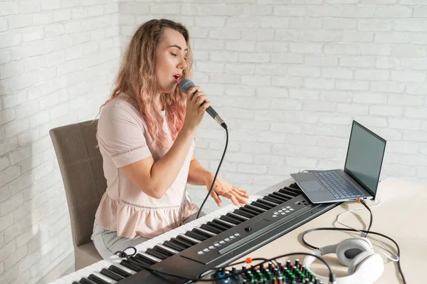 Eine Frau nimmt eine Gesangsstunde mit einem Laptop auf und begleitet sie zu Hause auf einem Keyboard. Die Lehrerin singt ein Lied ins Mikrofon und spielt elektronisches Klavier. Ein Blogger nimmt ein Video auf. — Stockfoto