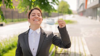 Memnun bir kadın sosyal mesafeyi korurken dışarı çıkar. Gülümseyen bir kadın ofis çalışanı maskesini çıkarma özgürlüğünün tadını çıkarıyor. Coronavirus yenildi. Çalışma gününün sonu..