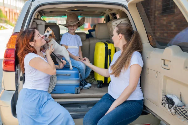 Glückliche gleichgeschlechtliche Familie auf einer Autofahrt durch das Land. Lesbisches Paar mit Sohn und Hund lädt Gepäck in den Kofferraum und ist bereit für den Sommerurlaub. Unabhängiges Reisen. — Stockfoto