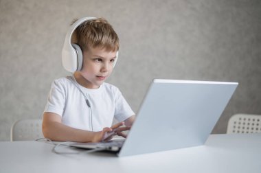 Sevimli Avrupalı çocuk kulaklıkla müzik dinliyor ve dizüstü bilgisayarında yazı yazıyor. Çocuk bilgisayarda ev ödevi yapıyor. Genç bir okul çocuğu uzaktan eğitim alır..