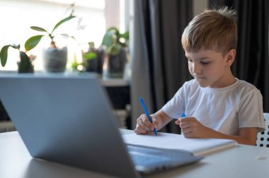 Çocuk dizüstü bilgisayardaki web kamerasından öğretmenle iletişim kuruyor. İnternetten ders. Karantinada uzaktan eğitim. Çalışkan bir öğrenci Coronavirus salgınında evde çalışıyor..