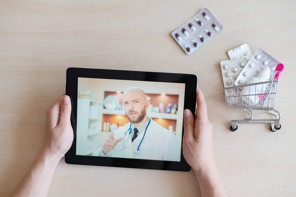 Professional male doctor on the screen of a digital tablet. Online appointment of a general practitioner. Mini medicine trolley. Remote consultation.