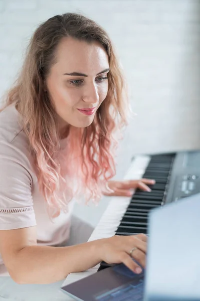 A friendly woman plays the electronic piano and conducts a video blog on her laptop. Stay home. Musical instrument teacher. Distance learning music quarantined.