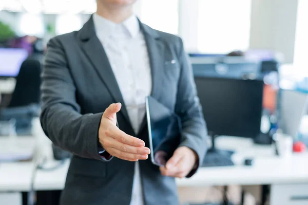 La trabajadora de oficina extiende su mano para saludarla. La dama de negocios sin rostro sostiene una tableta digital y un apretón de manos en un acuerdo para una transacción exitosa . — Foto de Stock