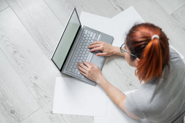 Top view of a freelancer working remotely while lying on the floor and typing on a laptop. Faceless woman shopping online from home. The student is preparing for the session.