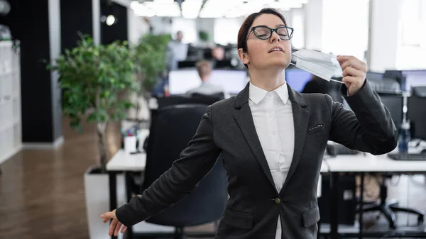 La mujer de negocios se quita la máscara en la oficina al final de la cuarentena. El coronavirus ha terminado. La chica respira libremente y cierra los ojos en el placer. Victoria sobre la pandemia . —  Fotos de Stock