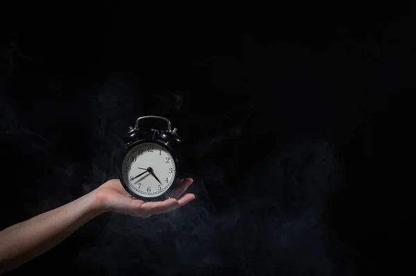 Una mujer sostiene un despertador en un estudio lleno de humo. Niebla blanca envolvió un reloj mecánico retro redondo . —  Fotos de Stock