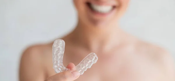 Primer plano del alineador de dientes transparentes de silicona ortodóncica en manos femeninas. Mujer borrosa irreconocible sostiene un retenedor de noche extraíble. Soporte para blanqueamiento de dientes para una sonrisa perfecta . —  Fotos de Stock
