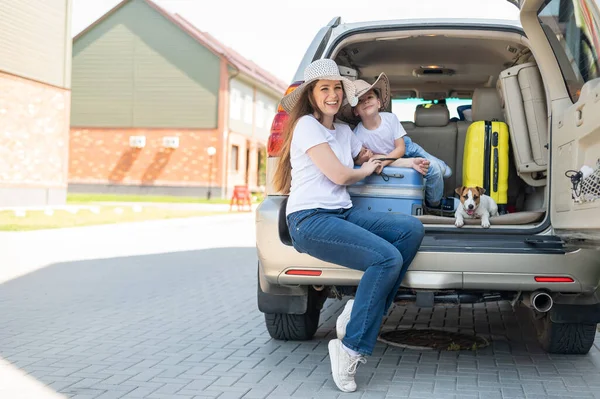 Europäische Alleinerziehende und Jack Russell Welpen reisen mit dem Auto. Kleinkind mit Mutter und kleinem Hund sitzen im Kofferraum und machen Sommerferien. Unabhängiger Familienausflug mit Kind. — Stockfoto