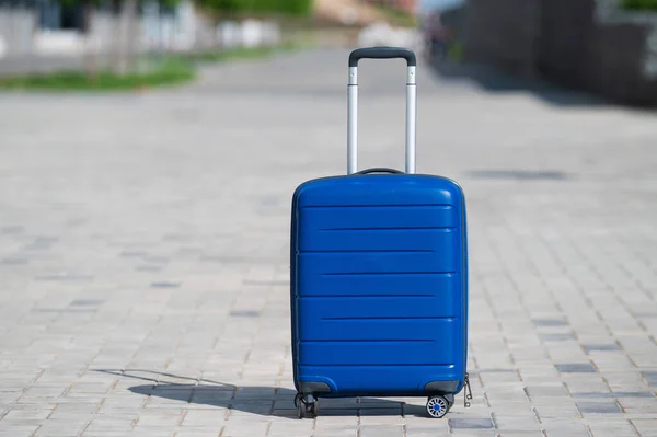 Blauwe koffer op wielen op de stoep. Bagage is in de straat van de stad en klaar om te reizen. Grote tas voor onderweg. Geen mensen.. — Stockfoto