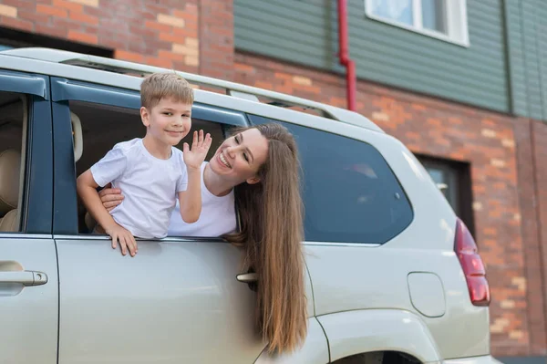 Glückliche Frau und Kind blicken aus dem Autofenster. Gut gelaunte Jungen sitzen mit ihrer Mutter auf dem Rücksitz des Autos und sind bereit für die Reise. Sommerferienkonzept. Familien-Roadtrip. — Stockfoto