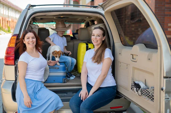 Glückliche gleichgeschlechtliche Familie auf einer Autofahrt durch das Land. Lesbisches Paar mit Sohn und Hund lädt Gepäck in den Kofferraum und ist bereit für den Sommerurlaub. Unabhängiges Reisen. — Stockfoto