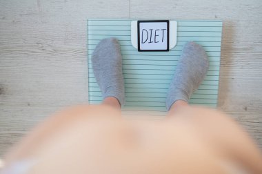 Yerdeki terazide duran çoraplı kadın bacaklarının üst görüntüsü. Diyet vitrinindeki yazı. Midesi ve obezitesi olan bir kadın kilo vermeli..