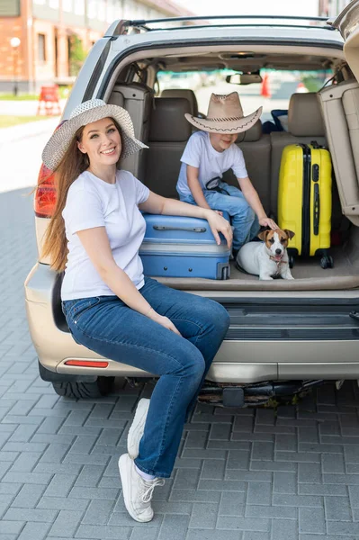 Europäische Alleinerziehende und Jack Russell Welpen reisen mit dem Auto. Kleinkind mit Mutter und kleinem Hund sitzen im Kofferraum und machen Sommerferien. Unabhängiger Familienausflug mit Kind. — Stockfoto