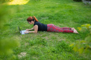 Kadın, parkta yeşil çimlerde yatarken dizüstü bilgisayarla alışveriş yapıyor. İki gözlüklü bir öğrenci çimlerin üzerinde yatarken kişisel kablosuz bilgisayarların başında çalışıyor. İnternetten alışveriş.