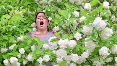 Güzel kızıl saçlı kadın hapşırır ve parkta çiçek açan bir elma ağacının yanında dururken burnunu ovuşturur. Mevsimsel alerjik rhinitis. Kızın polene alerjisi var..