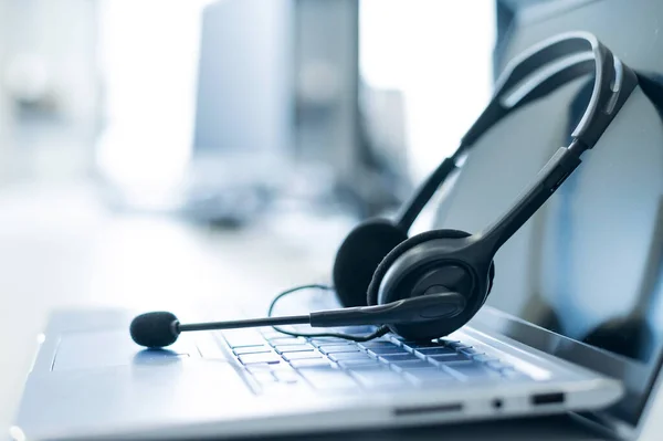 Escritorio del operador del centro de llamadas. Primer plano de un auricular en un portátil. Escritorio de ayuda. Lugar de trabajo de un empleado de servicios de apoyo. Auriculares con micrófono para VoIP en un teclado de ordenador. — Foto de Stock