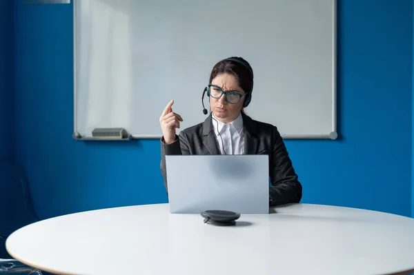 Una mujer enojada en un auricular está teniendo una conversación en línea en una computadora portátil en una sala de conferencias. Jefa regañando subordinadas para una videollamada. Negociaciones comerciales remotas infructuosas . —  Fotos de Stock