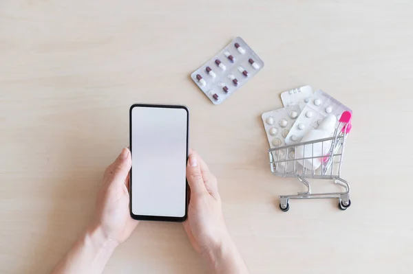 İlaçları uzaktan satın almak için mobil uygulama kavramı. İnternetteki eczane. Beyaz ekranlı, kadın eli akıllı bir telefon ve tablet kabarcıklı küçük bir tramvay..