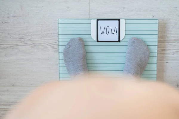 Κάτοψη των γυναικείων ποδιών σε γκρι κάλτσες σε κλίμακα δαπέδου. Η επιγραφή στην οθόνη wow. Μια παχύσαρκη γυναίκα μετράει το βάρος της. Γυμνή μεγάλη κοιλιά. — Φωτογραφία Αρχείου