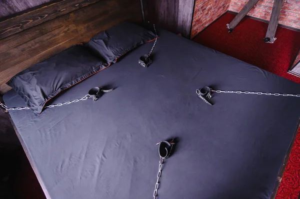 Schlafzimmer für intime Treffen. VDSM-Ausrüstung und Sexspielzeug. Lederhandschellen mit Kette auf einem grauen Laken. Fünfzig Grautöne. Fetisch-Dominanz. — Stockfoto