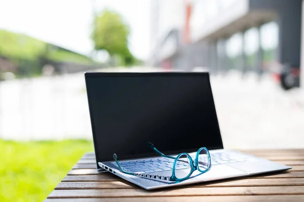 Close-up of glasses and laptop on a wooden table of a summer cafe. Freelancer workplace. Remote workplace. No people. — Stock Photo, Image