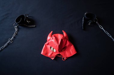 BDSM ekipmanları. Kırmızı deri bir şeytan maskesi ve gri bir çarşafta zincirli siyah kelepçeler. Seks oyuncakları. Hakimiyet. Kimse yok..
