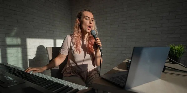 Een vrouwelijke blogger zingt en speelt live elektronische piano. Portret van een meisje dat een lied opneemt op een webcamera en componeert op een synthesizer. Online muzieklessen. Afstandsonderwijs in quarantaine. — Stockfoto