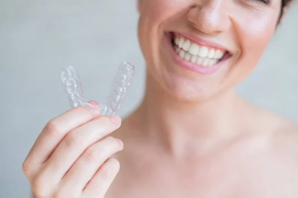 Close-up de dentes transparentes de silicone ortodôntico aligner em mãos femininas. Uma mulher com um sorriso charme perfeito detém um retentor de noite removível. Suporte para clareamento dos dentes. Foto cortada . — Fotografia de Stock