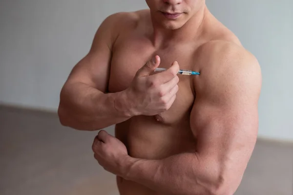 一个全身赤裸的肌肉男拿着毒品注射器。无法辨认的健美运动员把自己的类固醇。运动员因肌肉肿大而作弊. — 图库照片