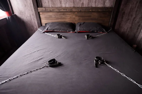 Bedroom for intimate meetings. VDSM equipment and sex toys. Leather handcuffs with a chain on a gray sheet. Fifty shades of gray. Fetish domination. — Stock Photo, Image