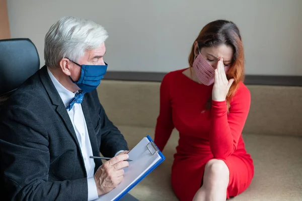 Male psychotherapist advises a female client in a medical mask. Moral support during the epidemic. Depressed woman on a visit to a psychologist. Treatment of panic attacks in the coronavirus.