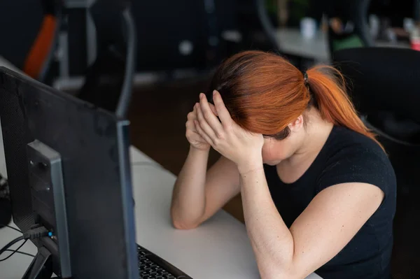 Trött kvinna arbetsnarkoman t-shirt i ett tomt kontor. Kvinnlig IT-chef i avslappnade kläder vid datorn. En tjej med huvudvärk jobbar övertid. Migrän och depression på grund av problem i arbetet — Stockfoto