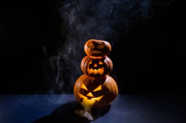 Karanlıkta korkunç bir balkabağı feneri piramidi. Balkabağına oyulmuş korkunç bir sırıtış. Geleneksel cadılar bayramı süslemeleri. Yatay tebrik kartı ya da pankart.