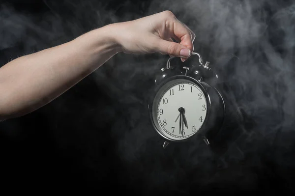 Una mujer sostiene un despertador en un estudio lleno de humo. Niebla blanca envolvió un reloj mecánico retro redondo . —  Fotos de Stock