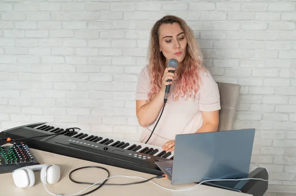 Egy nő felvesz egy hangórát egy laptoppal, és kíséri a billentyűzeten, miközben otthon van. A tanár énekel egy dalt a mikrofonba, és játszik az elektronikus zongorán. Egy blogger felvesz egy videót.. — Stock Fotó