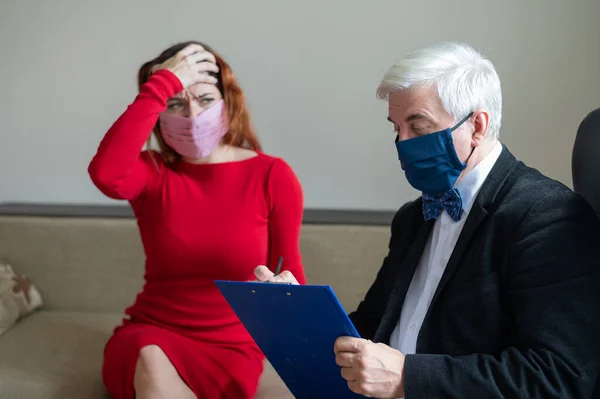 Male psychotherapist advises a female client in a medical mask. Moral support during the epidemic. Depressed woman on a visit to a psychologist. Hypochondria treatment.