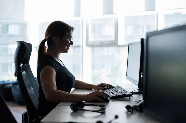Силуэт кавказской деловой женщины, печатающей за компьютером. Работница работает сверхурочно. Девушка сидит за столом в офисе одна. — стоковое фото