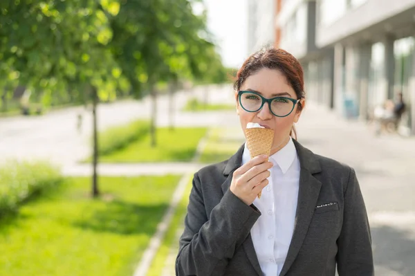 Obchodnice chodí po ulici a užívá si zmrzlinu. Šťastná dívka v obleku jí zmrzlinu kužel v horkém slunečném letním dni. Polední přestávka pro zaměstnance kanceláře. — Stock fotografie