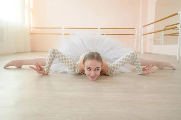 Beautiful ballerina in body and white tutu is training in a dance class. Young flexible dancer posing in pointe shoes sitting on the floor. — Stock Photo, Image