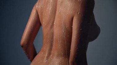 Beautiful naked female body with drops of milk on the skin. The girl in the shower. Water flows down a chic bust of a woman.