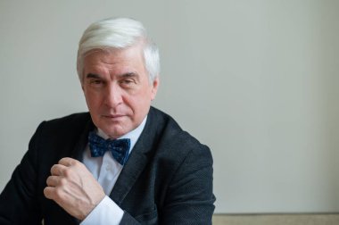 Takım elbiseli ve papyonlu, gri saçlı, gülümseyen bir adamın portresi. Zarif giyimli, temiz tıraşlı bir son sınıf öğrencisi kameraya özgüvenle bakıyor..