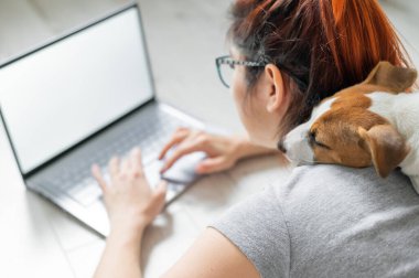 Tecritteki kızıl saçlı kadın yerde bir köpekle yatıyor. Kız sosyal mesafeyi koruyor ve bilgisayarla evden çalışıyor. Bayan öğrenci ev ödevi yapıyor. Koronavirüsün yayılması.